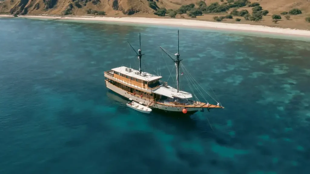 Komodo liveaboard anchored near Padar Island, surrounded by turquoise waters and scenic hills.
