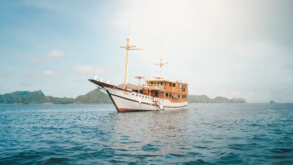 A luxurious Vinca Phinisi sailing through the pristine waters of Komodo National Park at sunset.